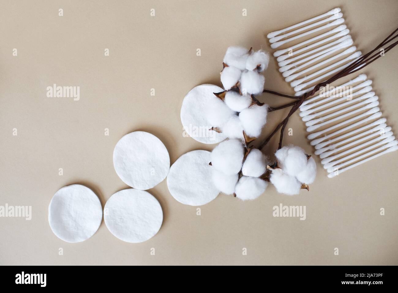 Flauschige Baumwollblumen-Wattestäbchen und Wattestäbchen auf beigem Hintergrund mit Platz zum Kopieren. Hygienisches Einwegprodukt Stockfoto