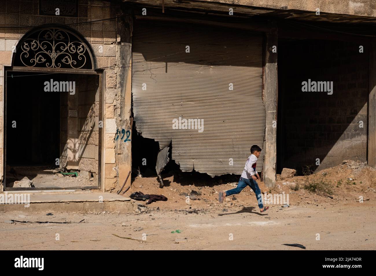 Darayya, Syrien - April, 2022: Kleiner Junge, der nach dem syrischen Bürgerkrieg auf der Straße in der zerstörten Stadt läuft. Stockfoto
