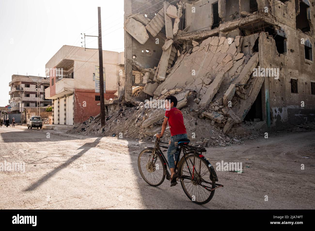 Darayya, Syrien - April, 2022: Kind auf dem Fahrrad auf der Straße in der zerstörten Stadt nach dem syrischen Bürgerkrieg. Stockfoto