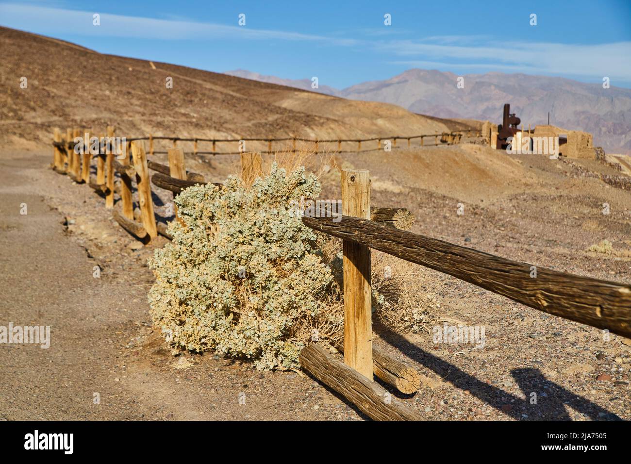 Death Valley Zaun für Pfad mit großem Strauch und alten Strukturen in der Ferne Stockfoto