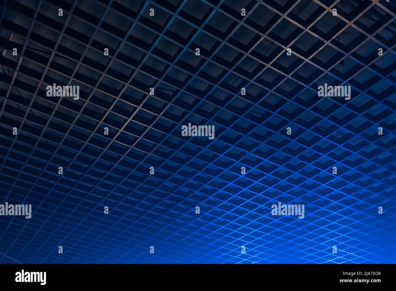 Deckengrill mit geometrischem Muster im Dunkeln mit abstraktem Interieur in blauem Neonlicht und Hintergrund mit sanftem Fokus. Stockfoto