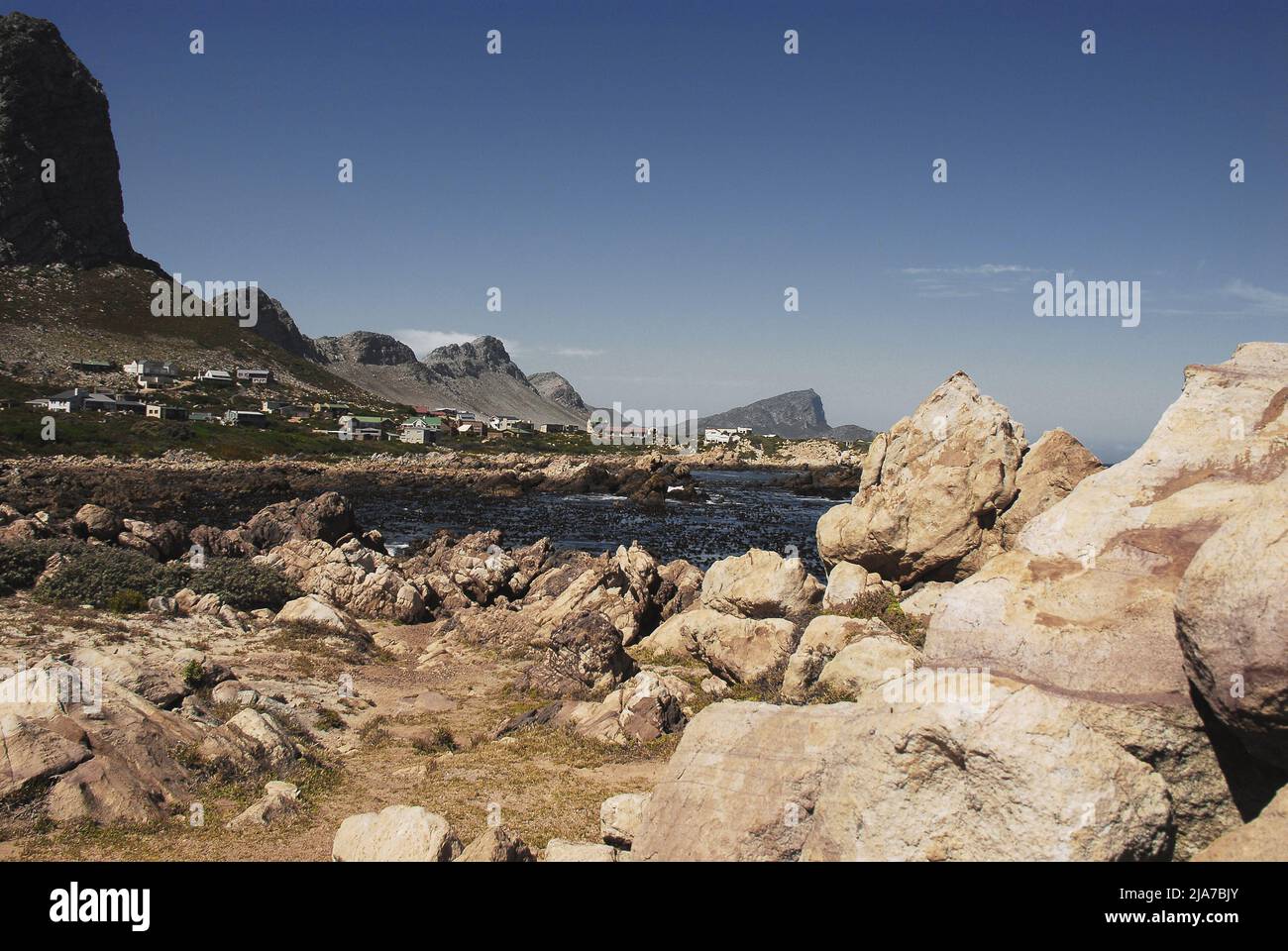 Panoramablick auf die Häuser in der Siedlung Rooi-Els zwischen hohen Bergklippen und der felsigen, zerklüfteten Küste Südafrikas. Stockfoto