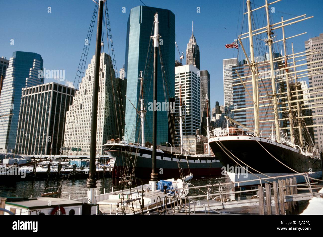 Wall Street in Downtown Manhattan hinter historischen Schiffen am Pier 17 am East River, New York City 1988 Stockfoto