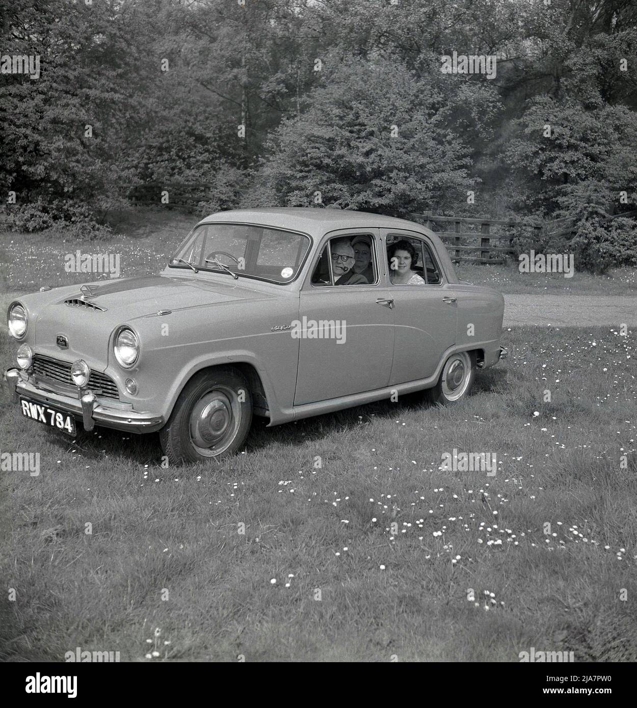 1950s, historisches Großbritannien nach dem Krieg, und parkte auf einem Feld in einem Park, ein Mann und zwei Damen saßen in einem Wagen der Ära Austin A40 in Cambridge. Der Herr raucht eine Pfeife, während die beiden Damen auf der Rückseite des 4-türigen kleinen Familienwagens sitzen. In dieser Zeit war es eine beliebte Freizeitbeschäftigung, einen Tag lang an einer malerischen Stelle zu fahren und gilt als das goldene Zeitalter des Autofahrens. Der vom britischen Hersteller Austin Motor Company hergestellte Austin Cambridge wurde von 1954 bis 1971 in verschiedenen Versionen und Karosserieformen produziert. Stockfoto