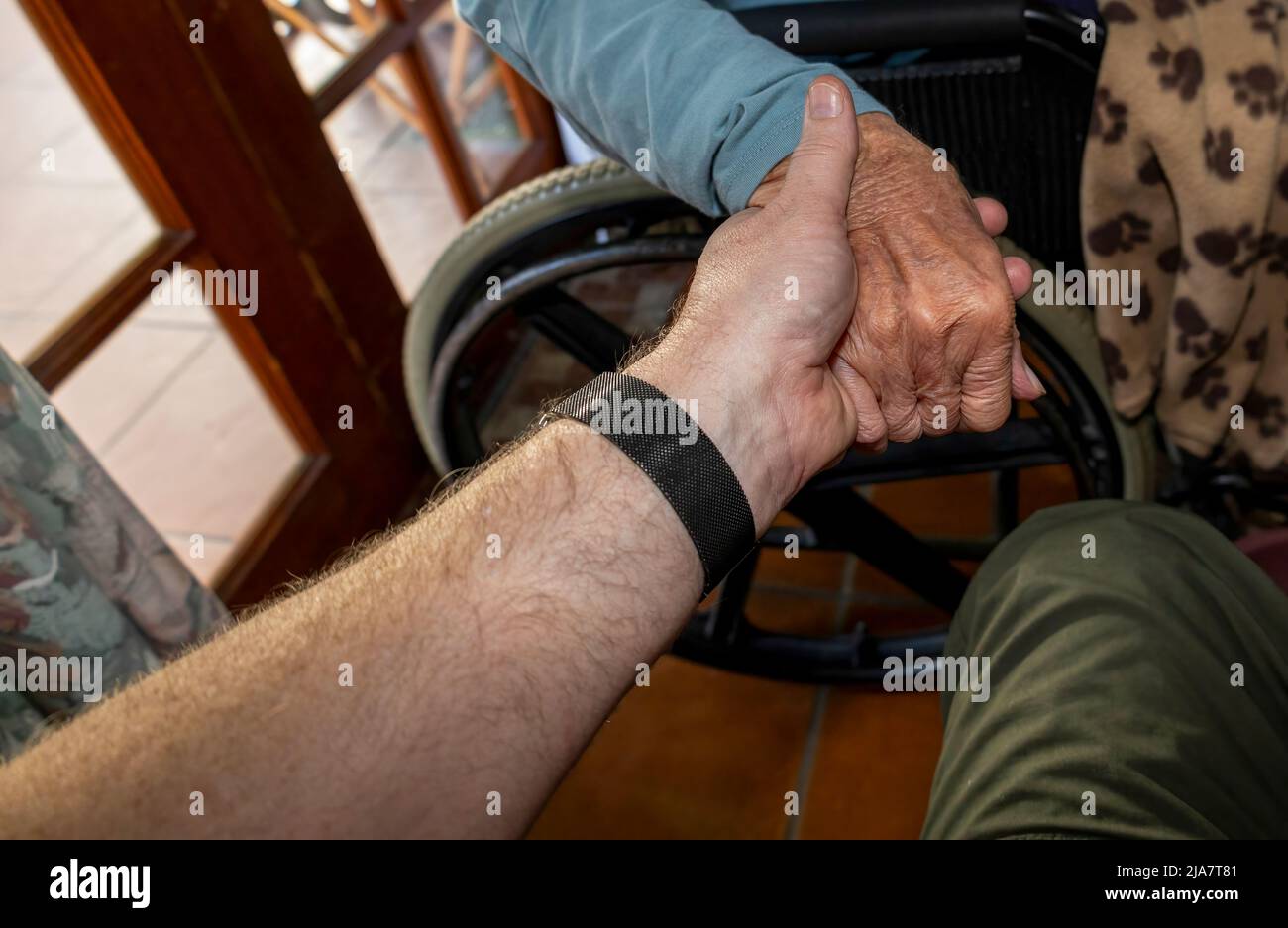 Ein Mann hält seine älteren Mütter lieblos in der Hand, während sie in einem Rollstuhl sitzt Stockfoto