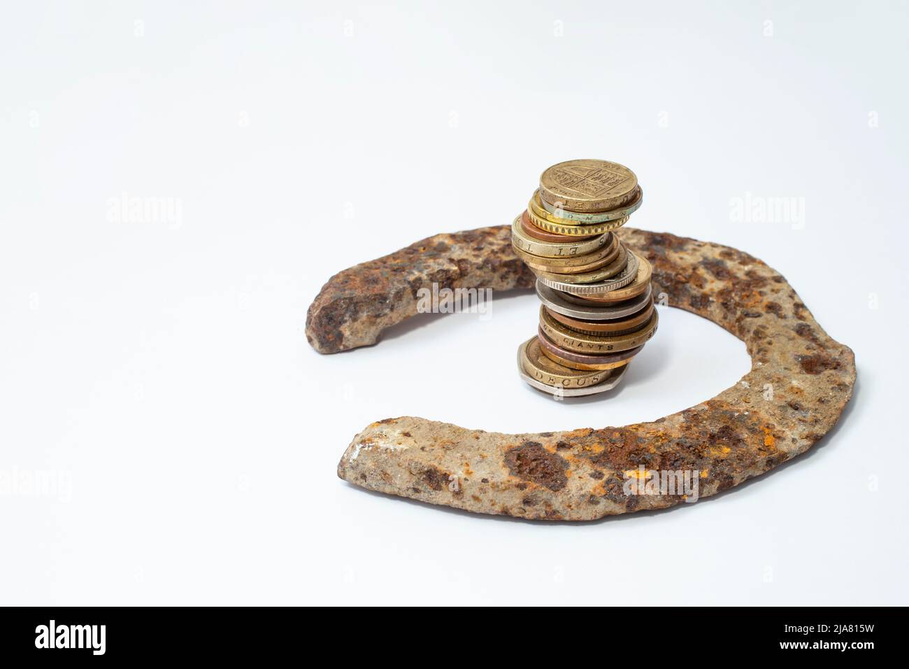 Rostiger alter Pferdeschuh mit einem hohen Münzstapel auf weißem Hintergrund, kreatives Konzept Stockfoto