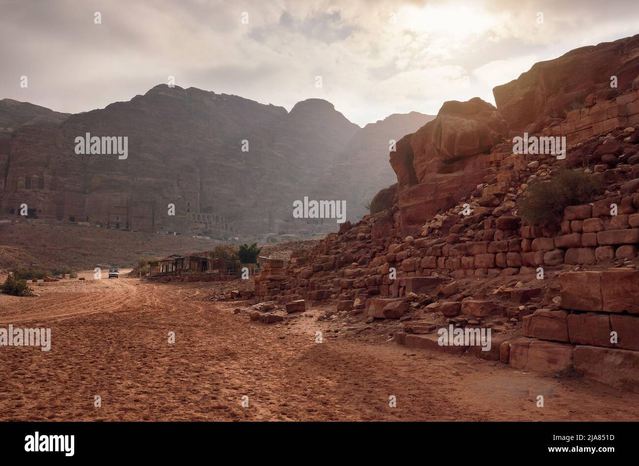 Typische Landschaft bei Petra, Jordanien, roter staubiger Boden, Berge mit geschnitzten Gebäuden in der Ferne Stockfoto