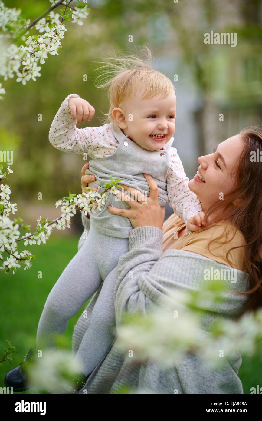 Mutter hält ein Baby in den Armen in einem blühenden Kirschgarten Stockfoto