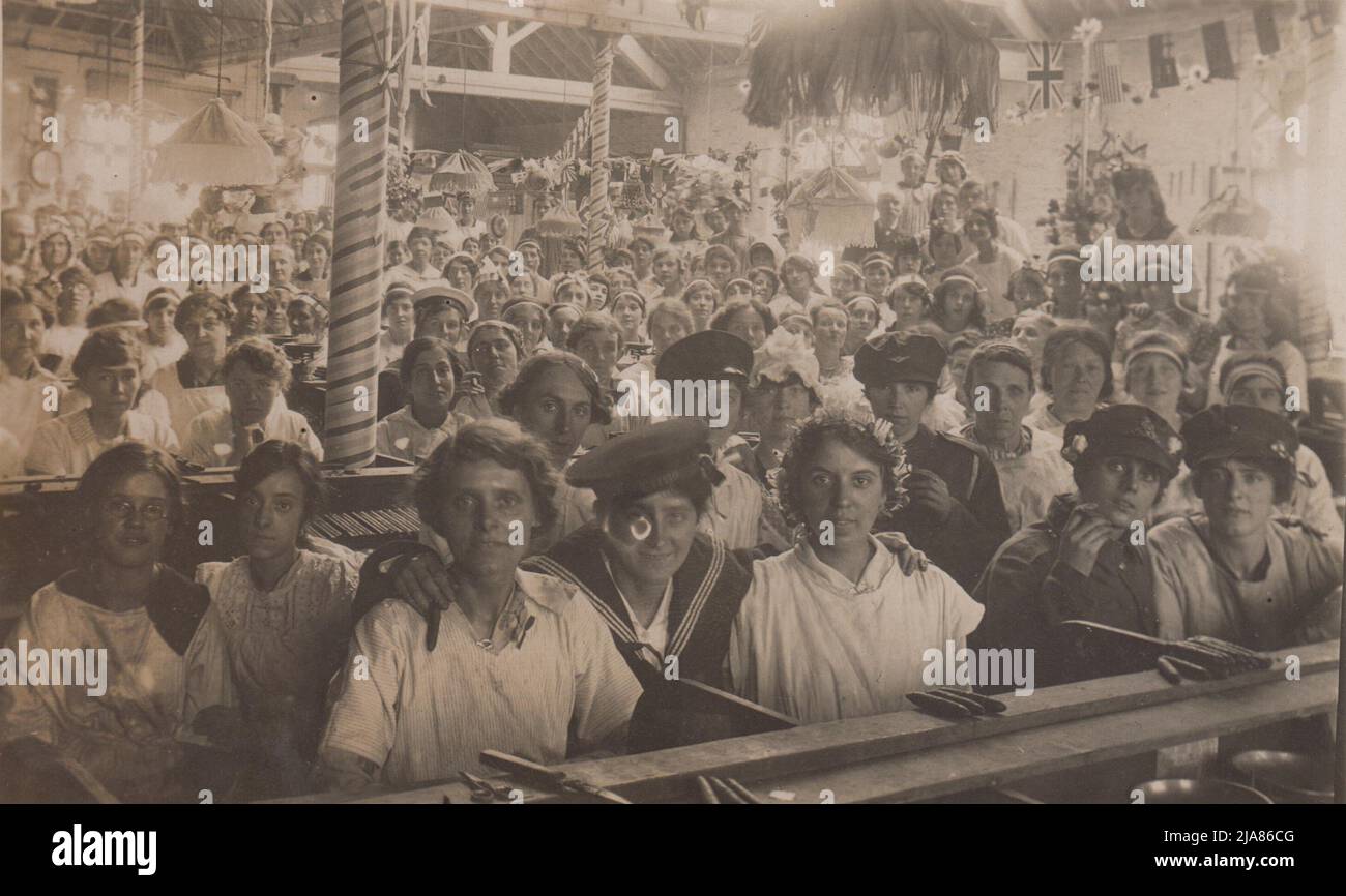 Zigarrenmacher versammelten sich im Zigarrenraum bei W.D. UND H.O. Wills, das Tabakunternehmen in Bristol, am Friedenstag (dem Ende des Ersten Weltkriegs). Das Foto zeigt eine große Gruppe von Frauen, viele junge, die sich hinter ihren Werkbänken versammelt haben. Mehrere sind in Matrosen- und Soldatenuniformen gekleidet und posieren mit Zigarren in den Händen. Auf den Sitzbänken vor ihnen sind auch gerollte Zigarren zu sehen. Der Workshop wurde mit Fahnen der Alliierten, darunter der Union Jack, geschmückt Stockfoto