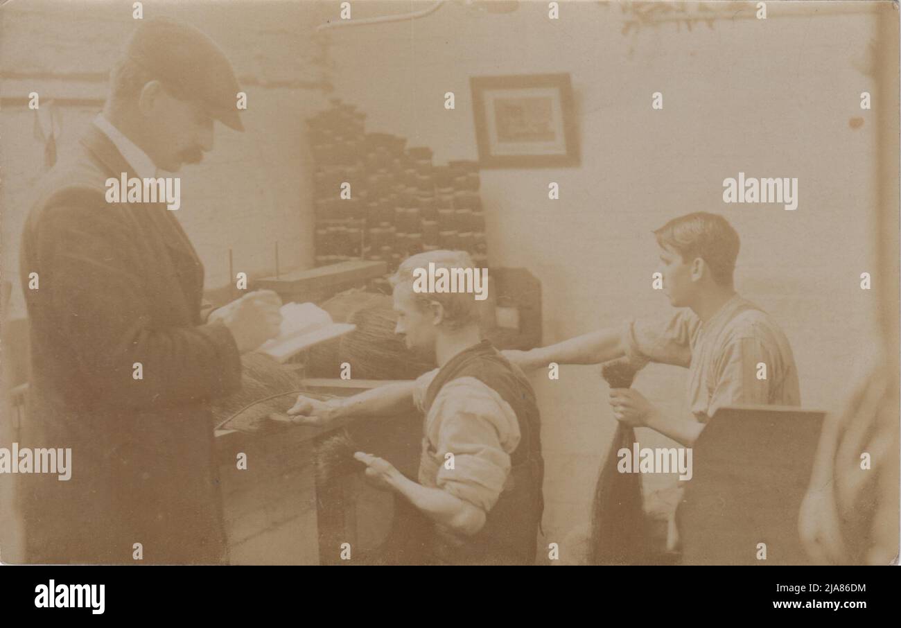 Wigmaker bei der Arbeit: Foto aus dem frühen 20.. Jahrhundert von drei Männern in einer Werkstatt, zwei haben große Hände voller langer Haare und sind dabei, Perücken zu machen, der dritte steht mit einem Notizbuch und überwacht Stockfoto