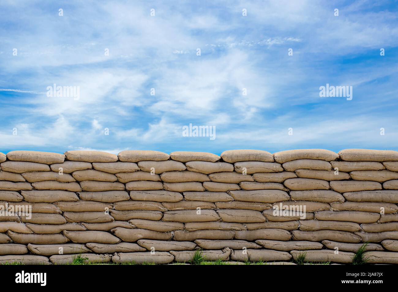 Ein Blick direkt auf eine Wand aus Sandsäcken. Blau schüchtern oben mit wispigen Wolken. Stockfoto