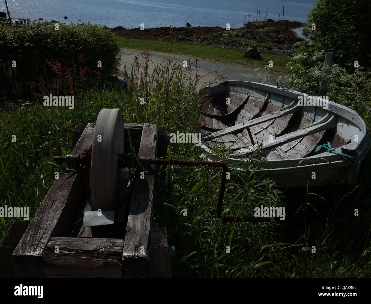 Ein alter Schleifstein und ein Ruderboot liegen tief im Gras am Ende von Moholmen. Mo i Rana, Norwegen. Stockfoto