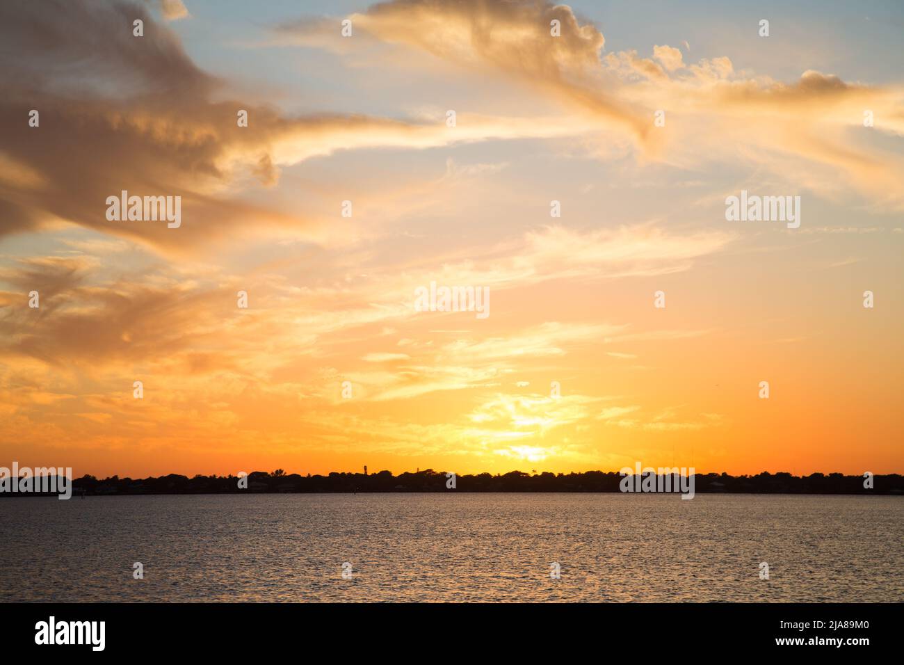 Phasen eines Sonnenuntergangs auf dem Meer mit der Sonne, die sich im Wasser spiegelt, Wolken am Himmel und einem Horizont, an dem das Wasser auf das Land trifft Stockfoto