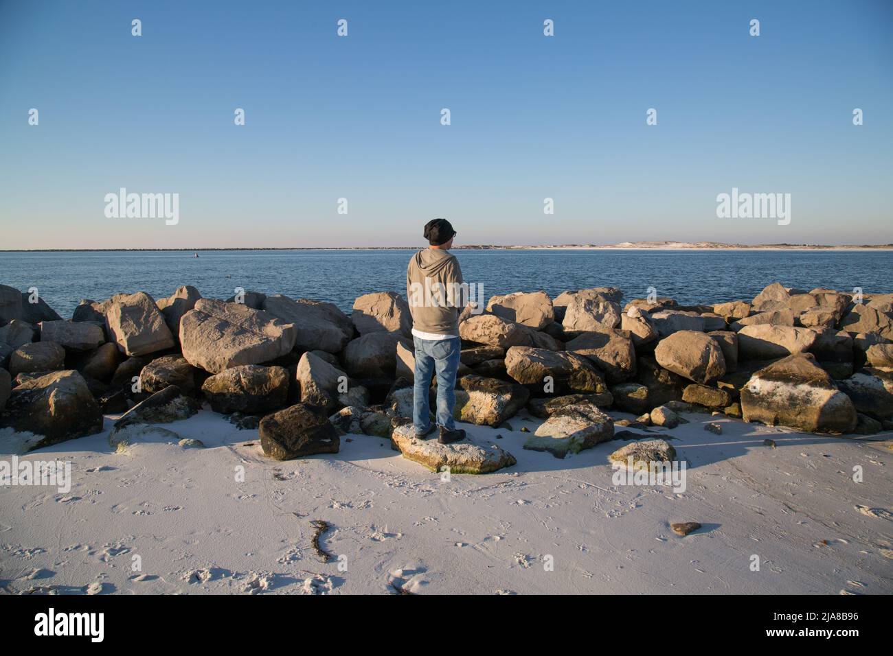 Ein Mann steht auf einem Felsen an einem Strand und blickt auf ein Riff im Meer Stockfoto