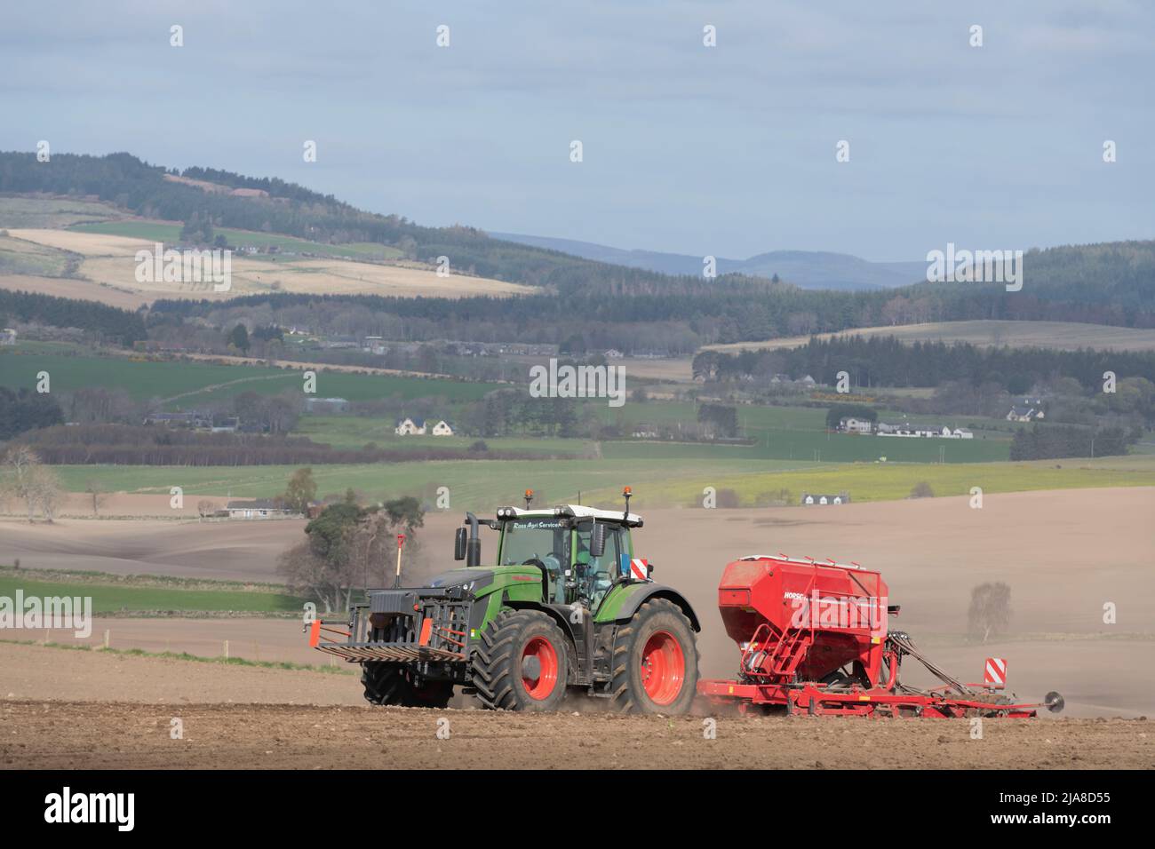 Ein Blick auf die Suie über eine Farmlandschaft in Aberdeenshire, mit einem grünen Fendt-Traktor und einem roten Saatbohrer, der Gerste auf dem nächsten Feld aussaat Stockfoto