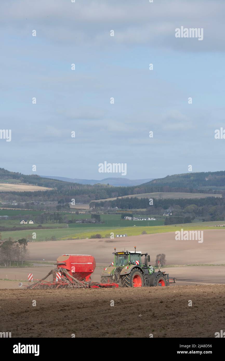 Ein landschaftlich reizvoller Blick über die Landschaft von Aberdeenshire im Frühling, mit einem Fendt-Traktor und einem Horsch-Sämaschine, die auf einem gepflügten Feld im Vordergrund arbeiten Stockfoto