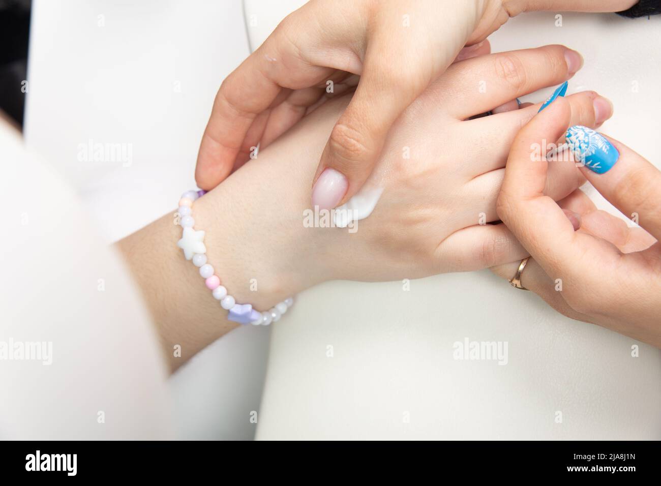 Eine Manikuristin trägt nach einer Hardware-Maniküre in einem Schönheitssalon Handcreme auf weibliche Hände auf. Herz auf die Hand gezogen, Handcreme. Die Creme auf y auftragen Stockfoto