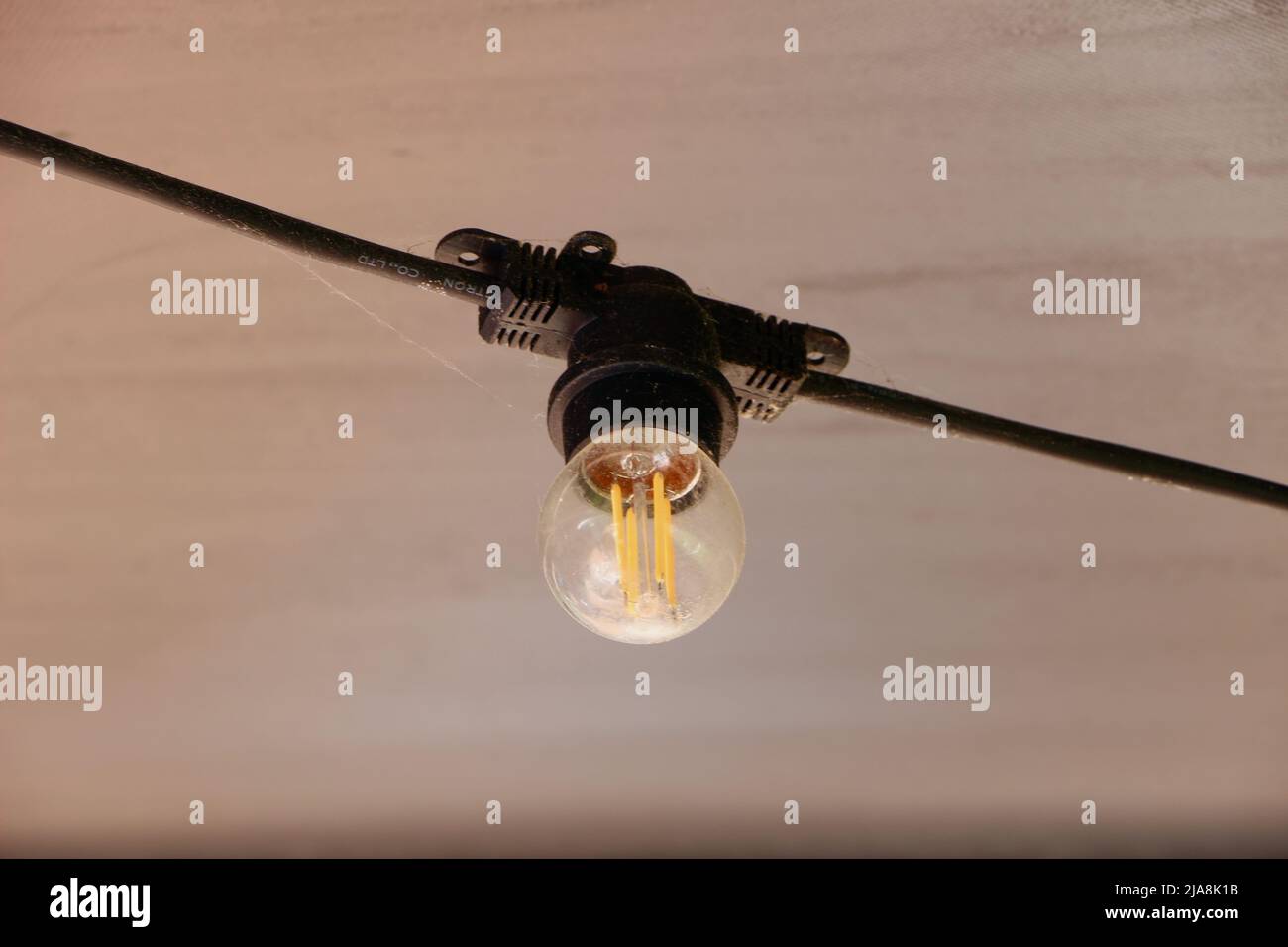 Eine runde, energieeffiziente LED-Glühlampe aus klarem Glas, die unter der Decke eines Terrassendachs des Restaurants hängt Stockfoto