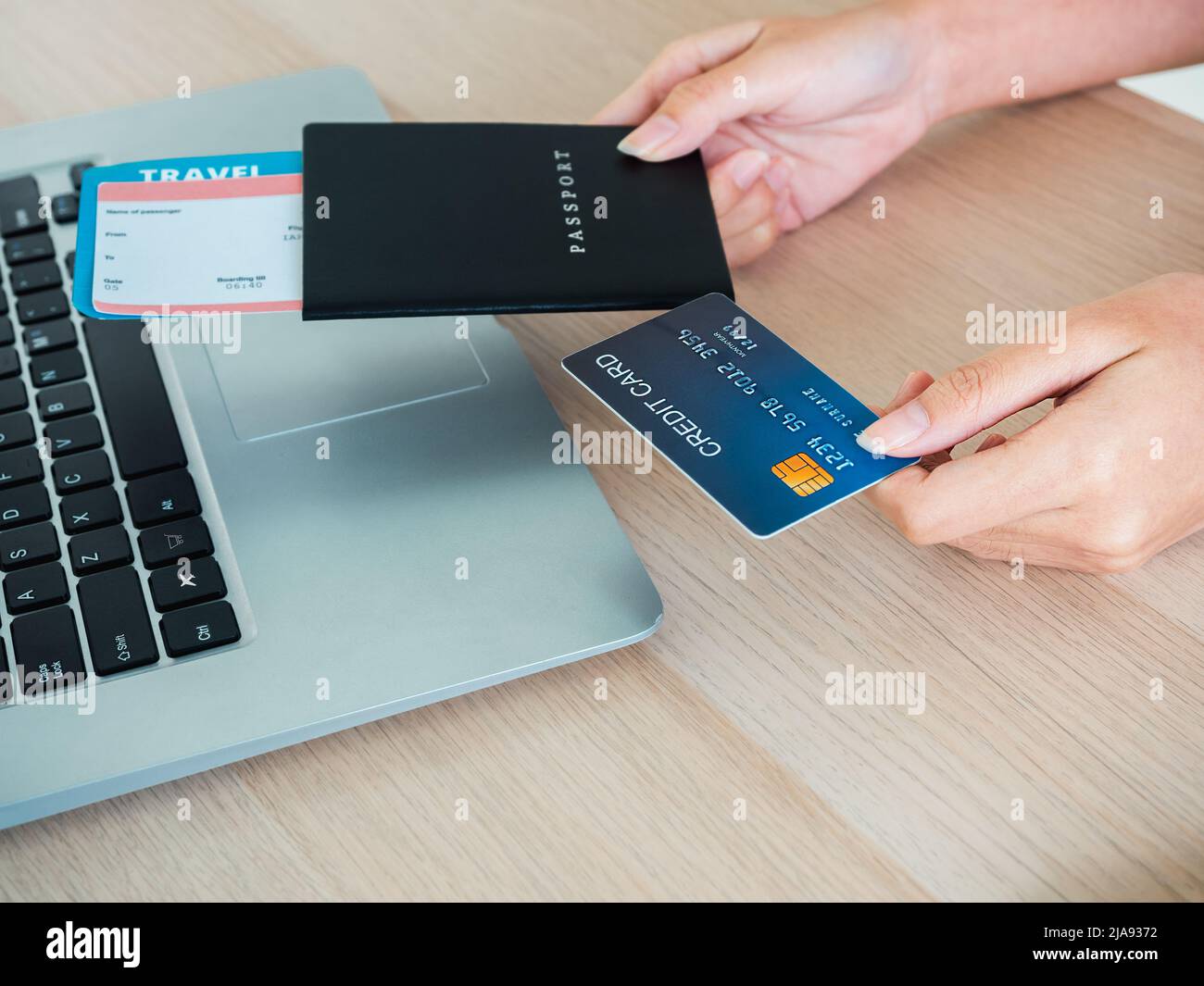 Die Hand der jungen Frau hält Kreditkarte und Reisepass, während sie den Laptop für die Flugbuchung benutzt, das Hotelzimmer für die Sommerreise auf dem Tisch, bereit für die Reise Stockfoto