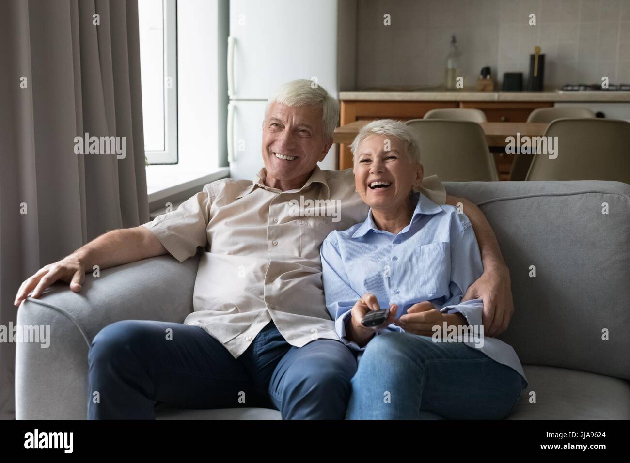 Lachende ältere Ehepartner kuscheln auf der Couch und sehen sich tv-Filmkomödie an Stockfoto