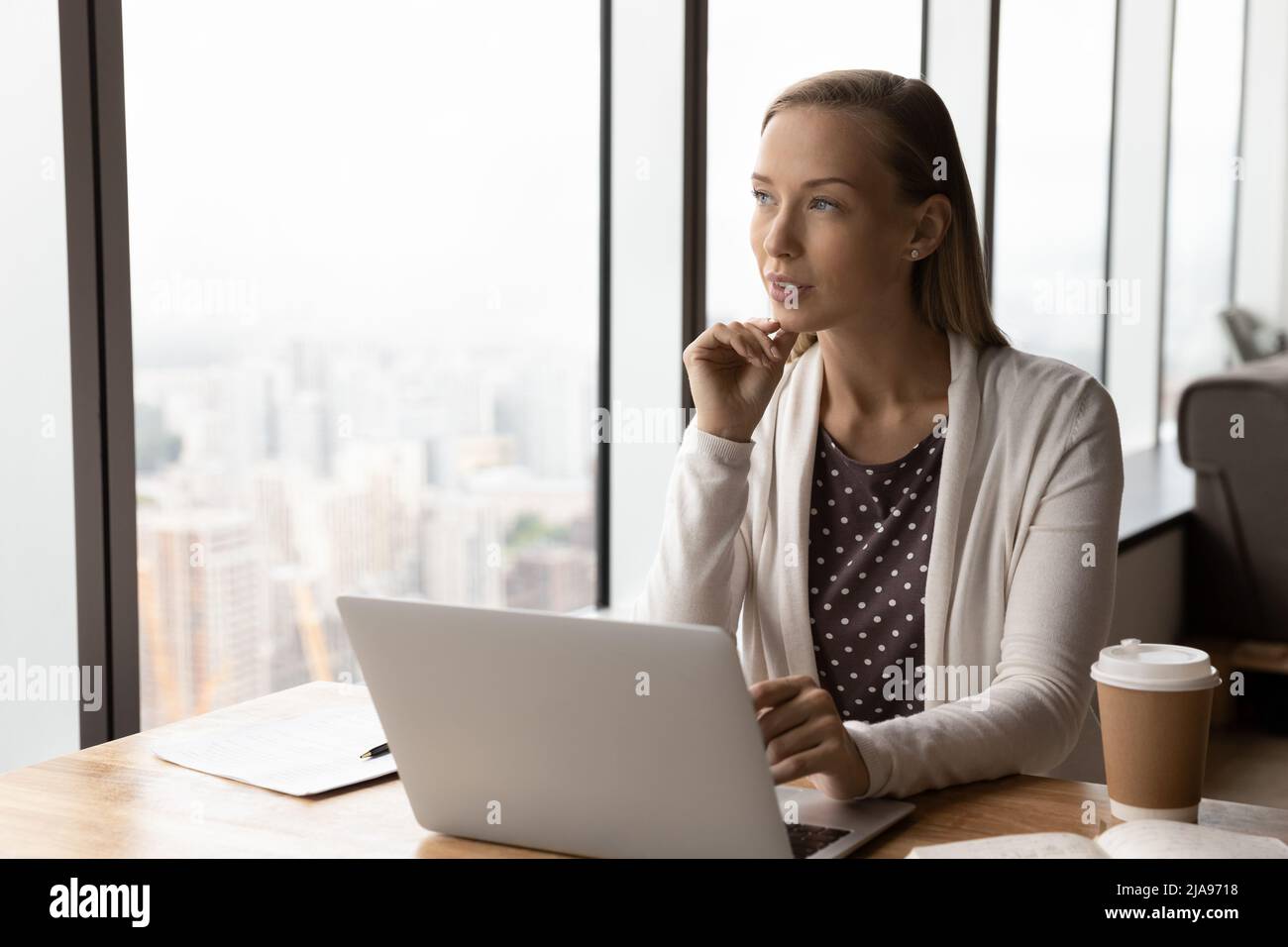 Durchdachte Geschäftsfrau, die mit einem Laptop über ein Projekt am Arbeitsplatz nachdenkt Stockfoto