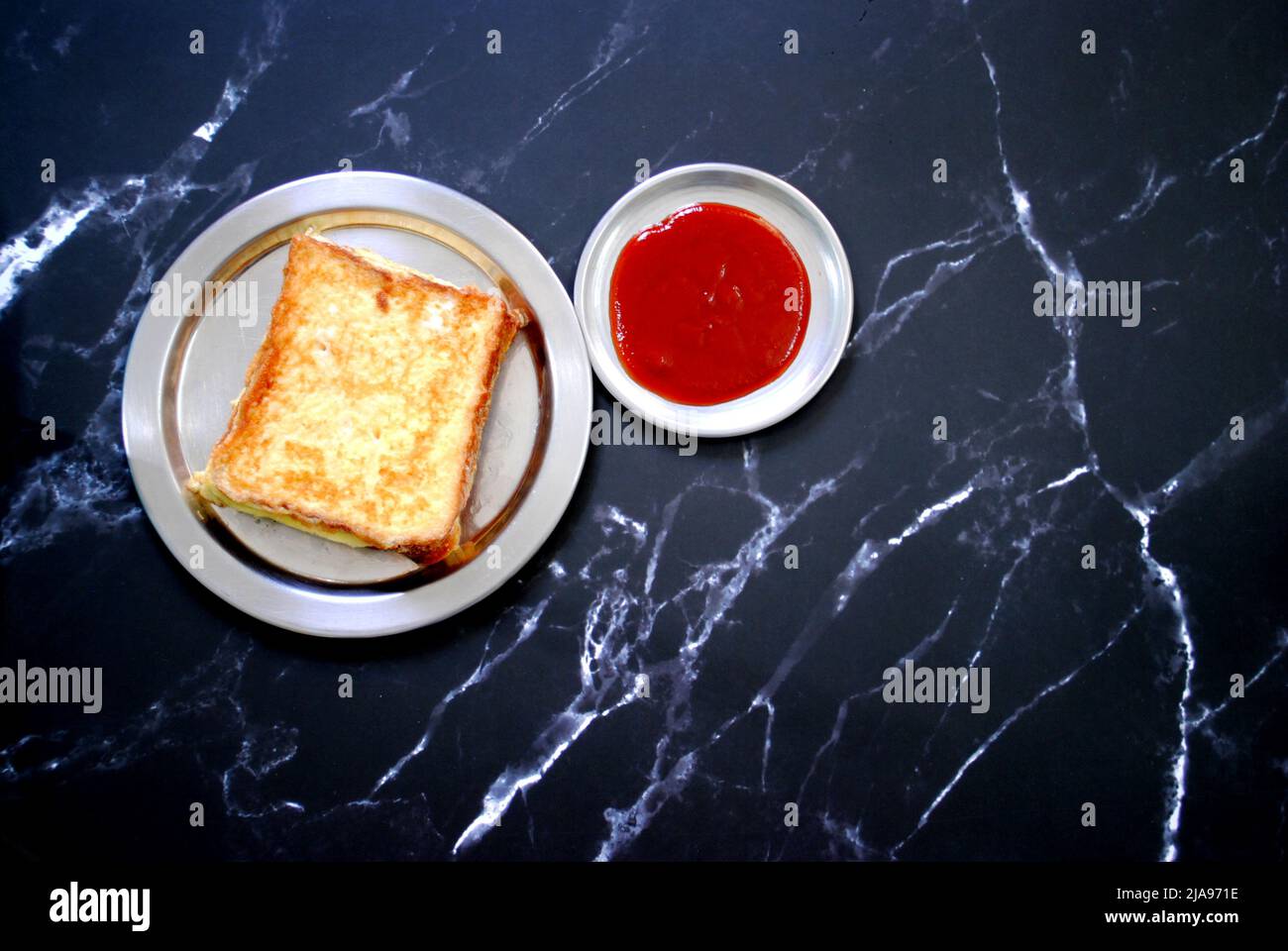 Frisch gekochtes Brot Omelett und rote Tomatensauce werden auf einem silbernen Teller mit schwarzem Hintergrund platziert und fertig zum Servieren Stockfoto