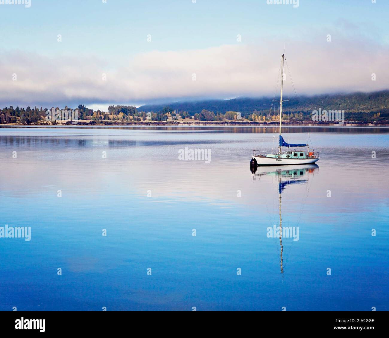Neblige friedliche Szene am frühen Morgen mit einem Segelboot mit Spiegelung im stillen Wasser am Lake Te Anau, Neuseeland-Südinsel. Stockfoto