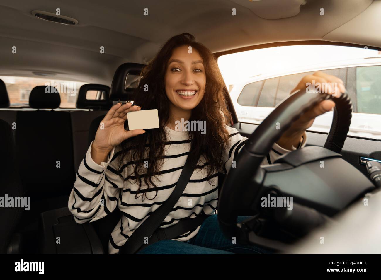 Lächelnde Frau, die ein neues Auto fährt und den Führerschein zeigt Stockfoto