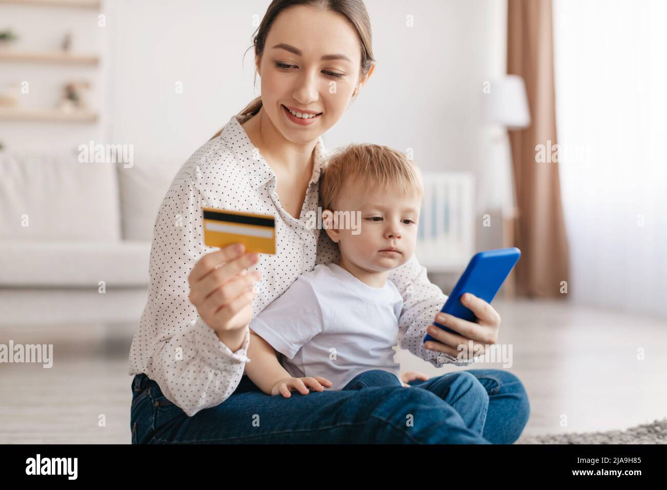 Positive junge Mutter und entzückender Kleinkind Sohn online zusammen einkaufen, halten Kreditkarte und mit dem Smartphone Stockfoto