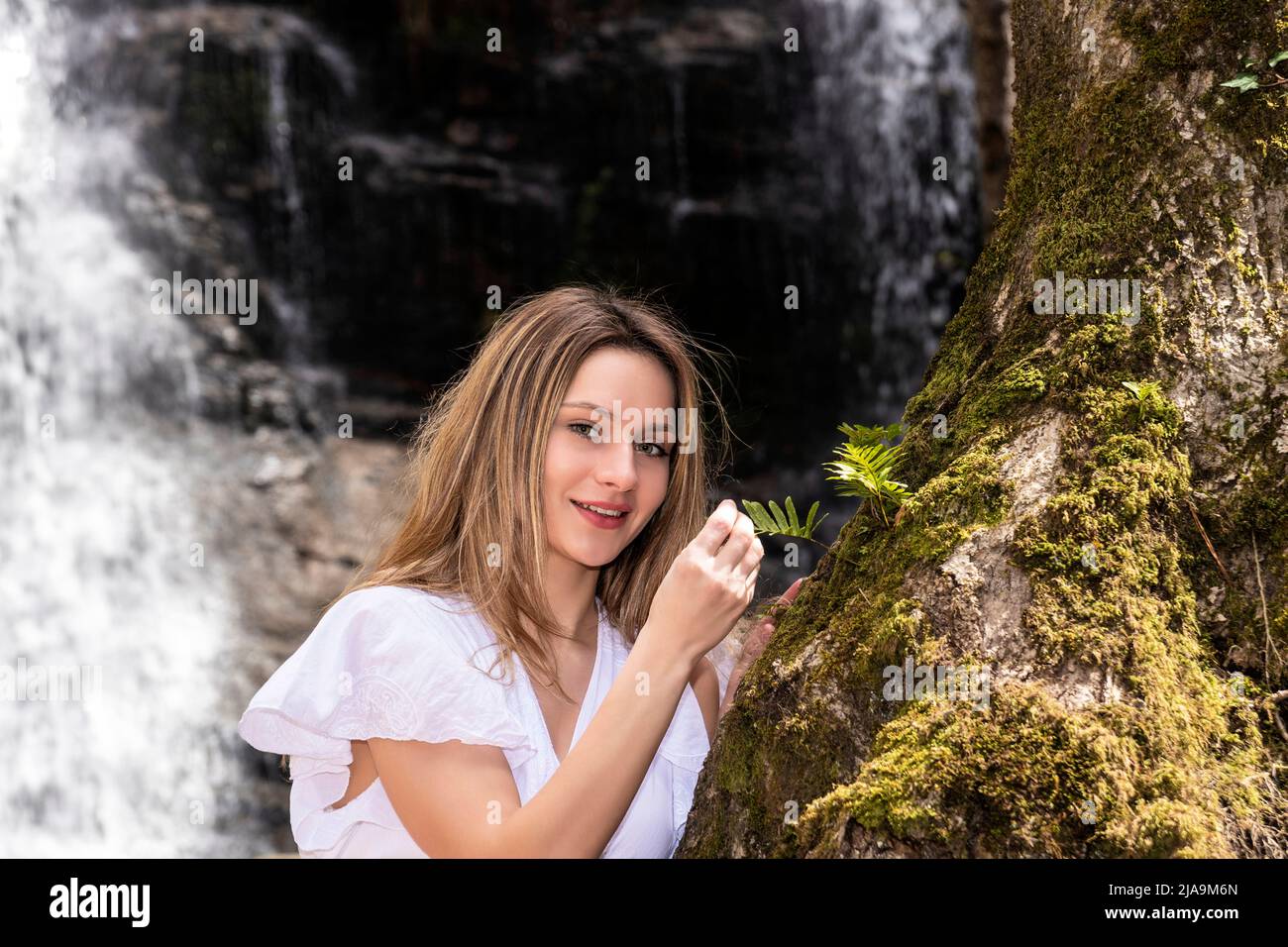 Lächelnde blonde Frau im Wald mit einem Wasserfall Stockfoto