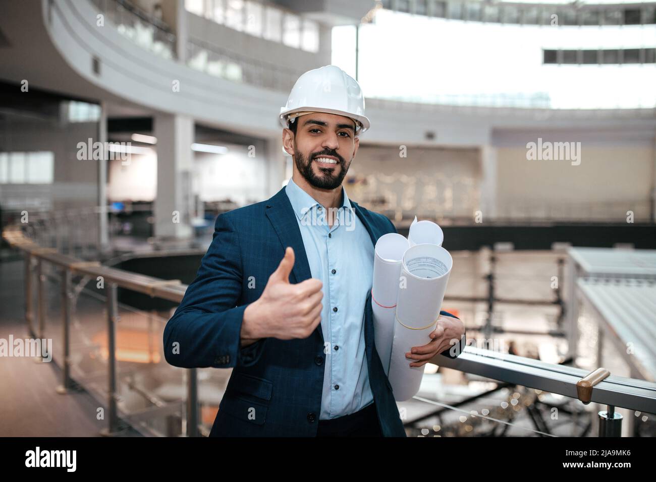Frohes Vertrauen tausendjährigen islamischen Kerl Ingenieur in Schutzhelm, Anzug mit Bart mit Projektzeichnungen Stockfoto