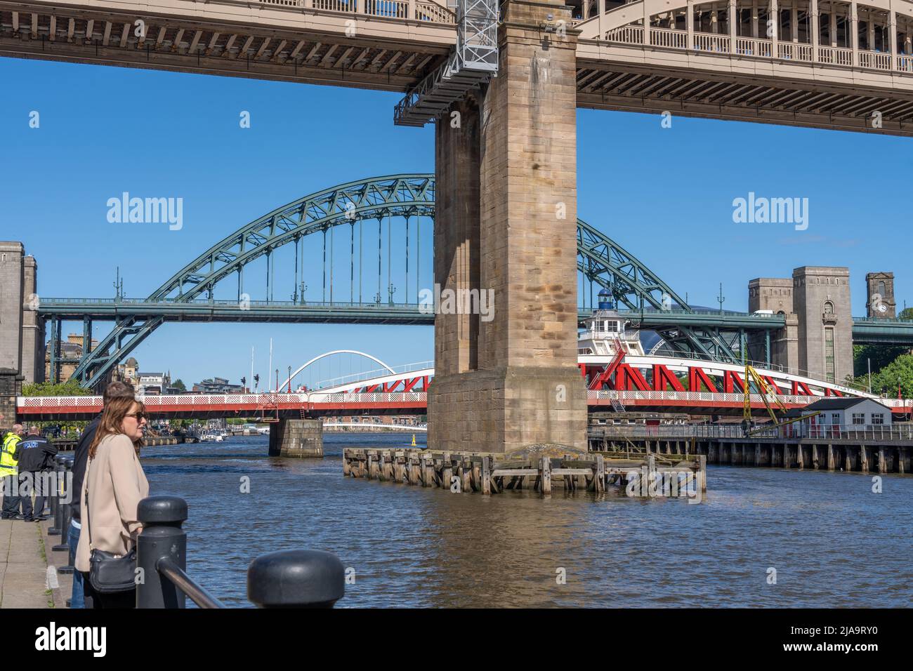 An einem blauen Tag blicken die Menschen über den Fluss Tyne und vier seiner Brücken am Kai, Newcastle upon Tyne, Großbritannien. Stockfoto