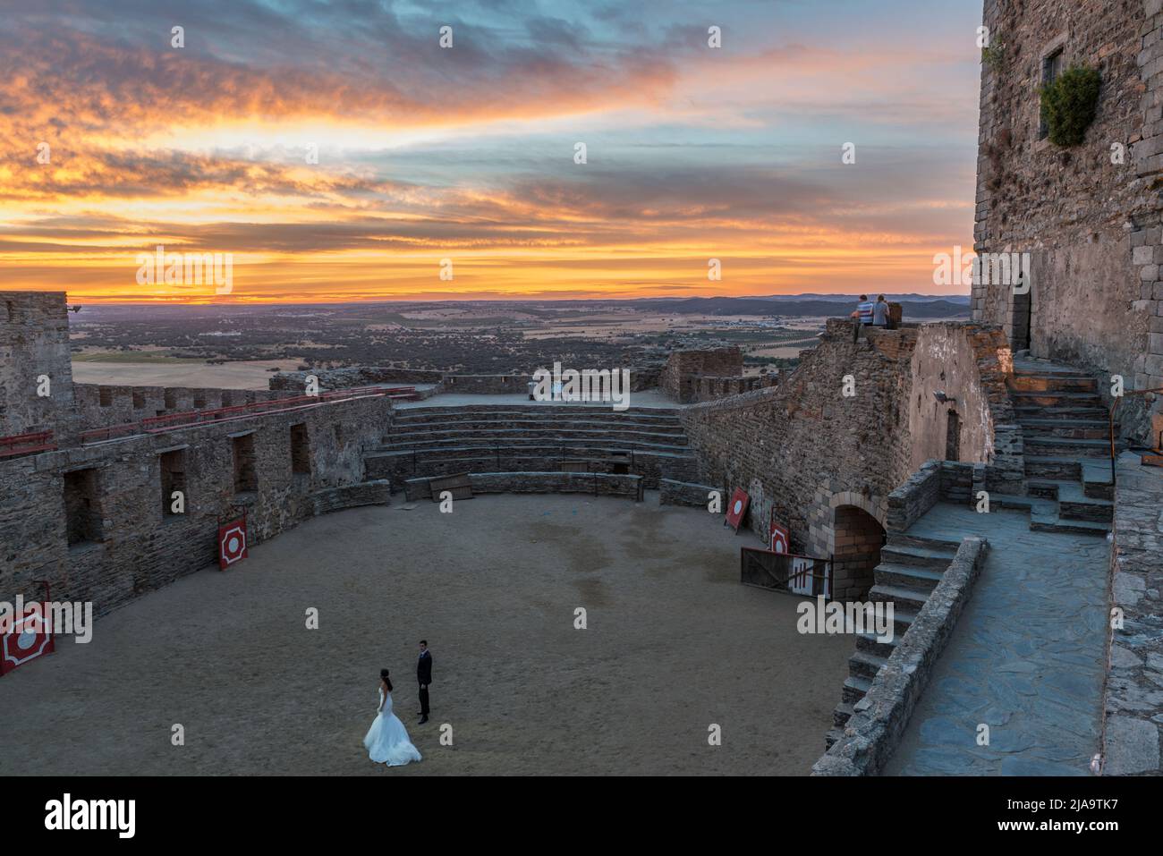 Ein Brautpaar bereitet sich auf ein Fotoshooting in der Mitte der Arena des Schlosses von Monsaraz bei Sonnenuntergang, Alentejo, Portugal, vor. Stockfoto