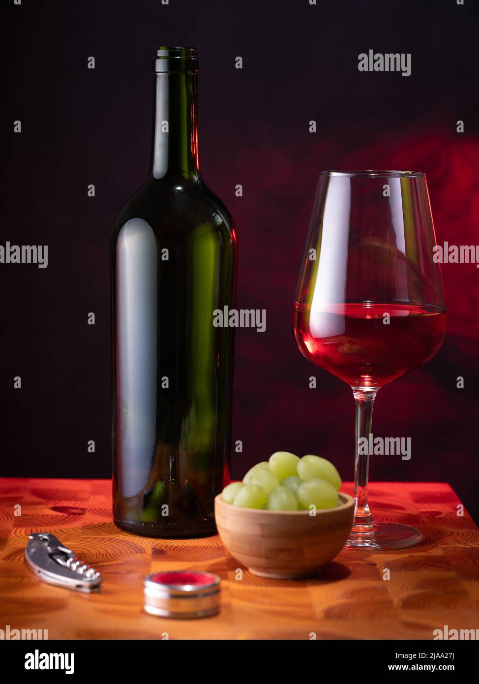 Helsinki / Finnland - 29. MAI 2022: Eine leere Rotweinflasche, ein Glas Wein und einige Trauben auf einer Holzfläche vor dunklem Hintergrund. Stockfoto