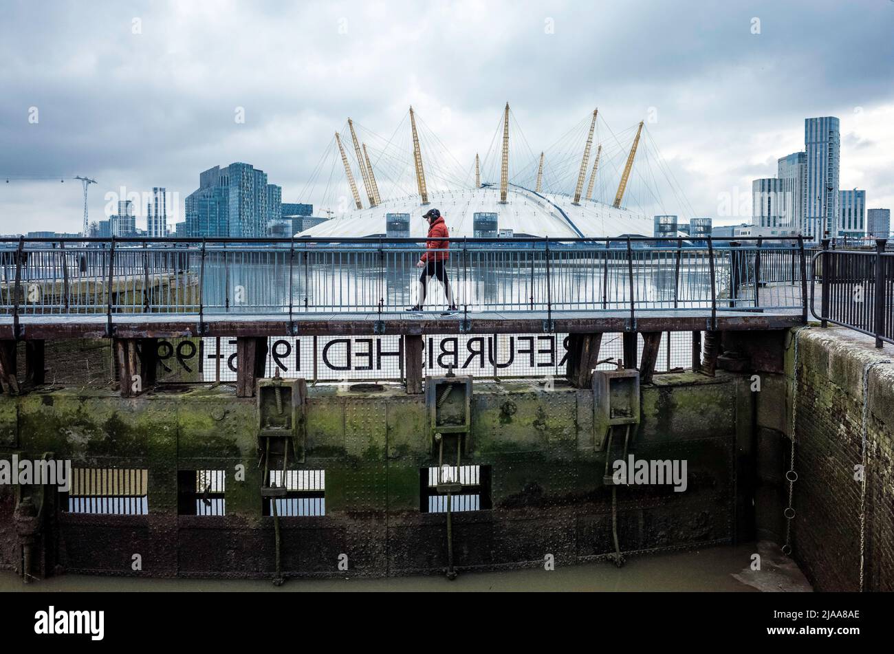 Der Mensch geht über den Beckensteg des East India Dock mit der Themse und der O2 Arena im Hintergrund. Stockfoto