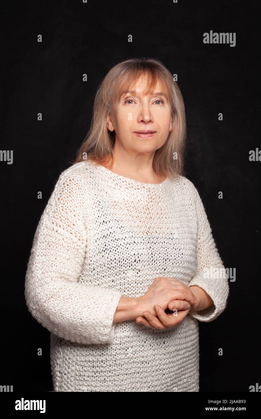 Ältere Frau im mittleren Alter, lächelnd und vor schwarzem Hintergrund der Studiowand stehend Stockfoto