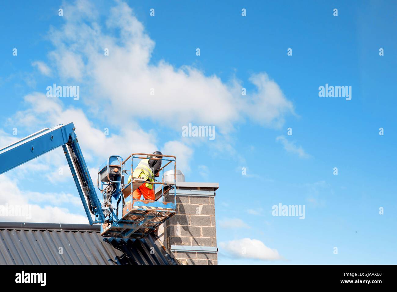 Bauherren, die vom Teleskopausleger-Lift aus arbeiten, montieren wärmegedämmte Sandwichpaneele an der Fassade eines neuen mehrstöckigen Wohngebäudes. Wo Stockfoto