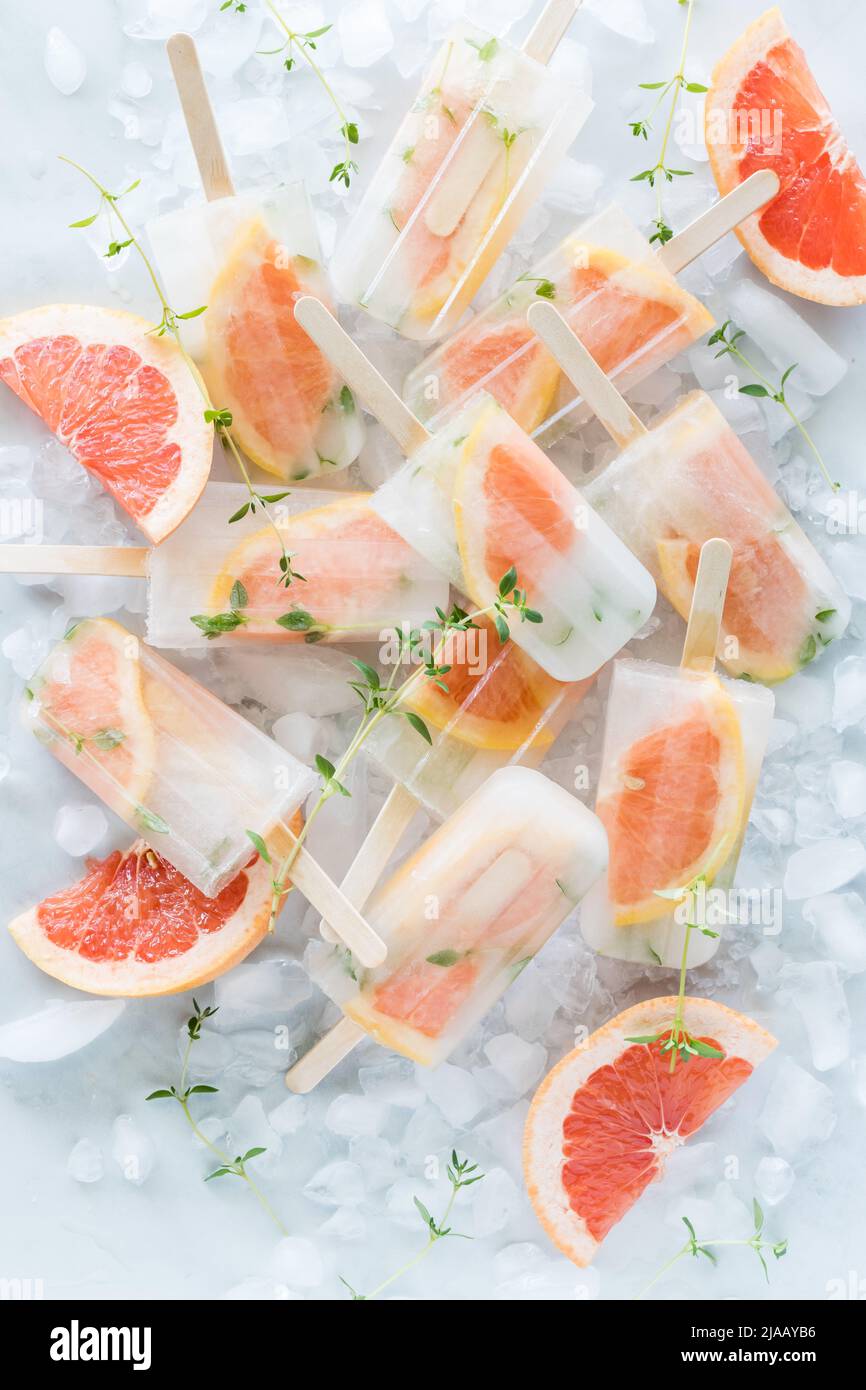 Ein Haufen erfrischender eisiger, kalter Grapefruit-Thymianpopsicles auf Eiswürfeln. Stockfoto