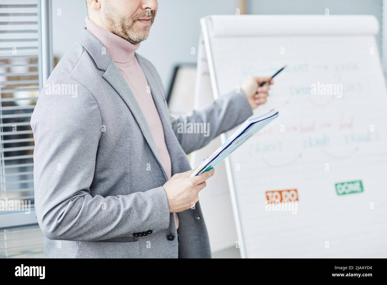 Ausgeschnittene Aufnahme eines reifen Mannes, der im Büro Englischunterricht erteilt und auf das Whiteboard zeigt und Platz zum Kopieren verwendet Stockfoto