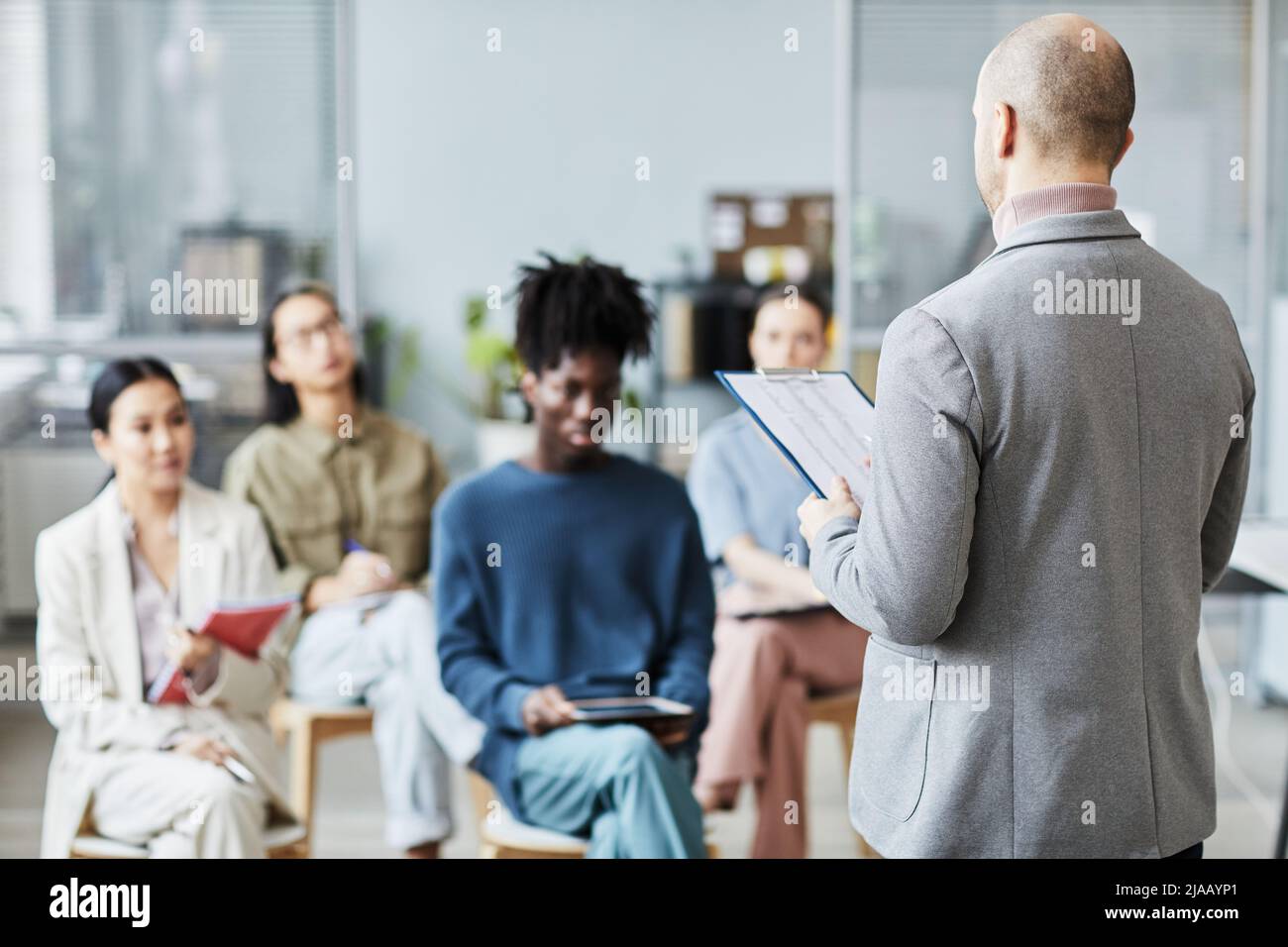 Rückansicht eines reifen männlichen Coaches, der im Büro eine Vorlesung oder ein Seminar für verschiedene Gruppen von Menschen hält, Raum kopieren Stockfoto