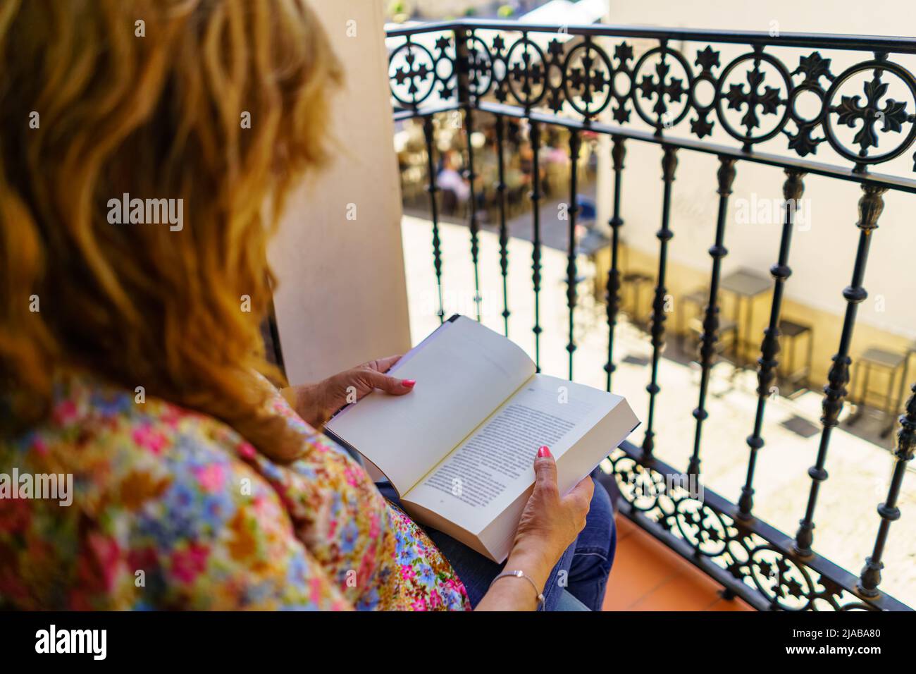 Eine Frau auf ihrem Rücken, die an einem sonnigen und heißen Tag ein Buch auf der Terrasse ihrer Häuser liest. Stockfoto