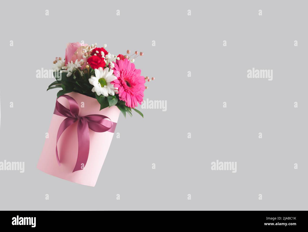 Rosa Geschenkbox mit verschiedenen bunten Blumen auf grauem Hintergrund. Valentinstag ästhetische Natur Konzept. 8 März Karte Idee. Stockfoto