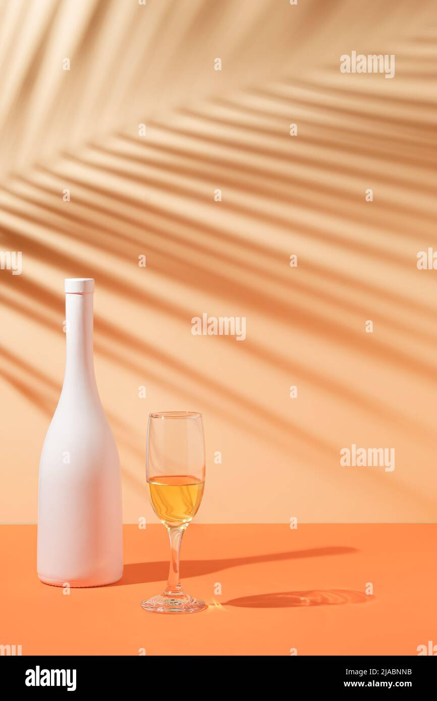 Draufsicht auf tropischen Blattschatten, weiße Flasche und Weinglas auf orangefarbenem Hintergrund. Tropische Sommerfeier. Stockfoto