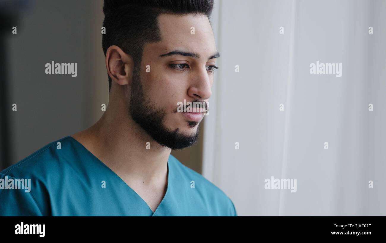 Junge nachdenkliche hispanische Arzt männlich nachdenklich arabischen Krankenschwester Praktiker Therapeut Chirurg stehen in der Nähe Fenster im Krankenhaus Arbeitsplatz warten auf Patienten Stockfoto