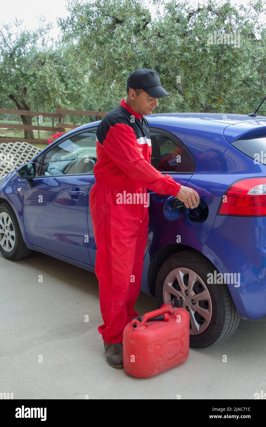Bild eines Mechanikers in Overalls, als er einen Zusatzstoff in den Tank eines Autos gießt. Verweis auf teuren Kraftstoff Stockfoto