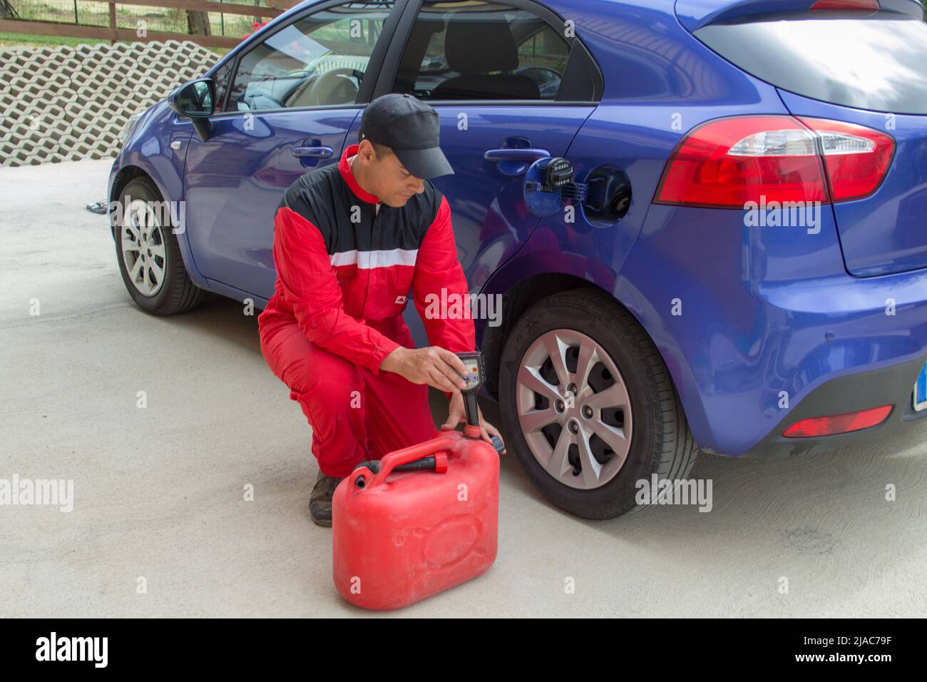 Bild eines Mechanikers in Overalls, als er einen Zusatzstoff in den Tank eines Autos gießt. Verweis auf teuren Kraftstoff Stockfoto