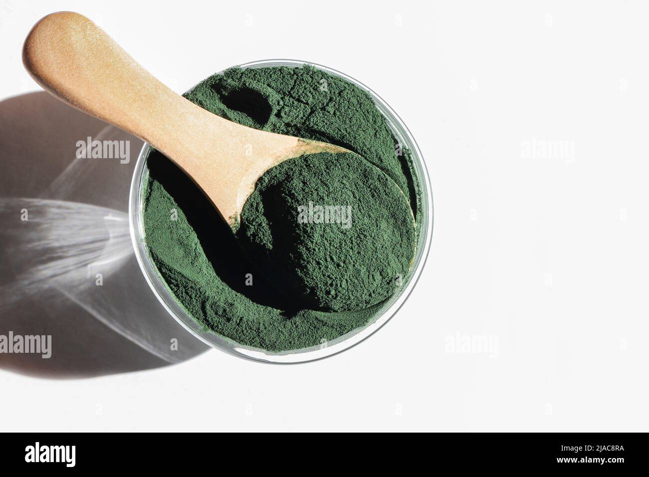 Natürliche Zusatzstoffe und Superfood. Grünes Spirulina Algenpulver im Glas mit Holzlöffel auf weißem Hintergrund. Gesundes Lifestyle-Konzept. Bio-Lebensmittel Stockfoto