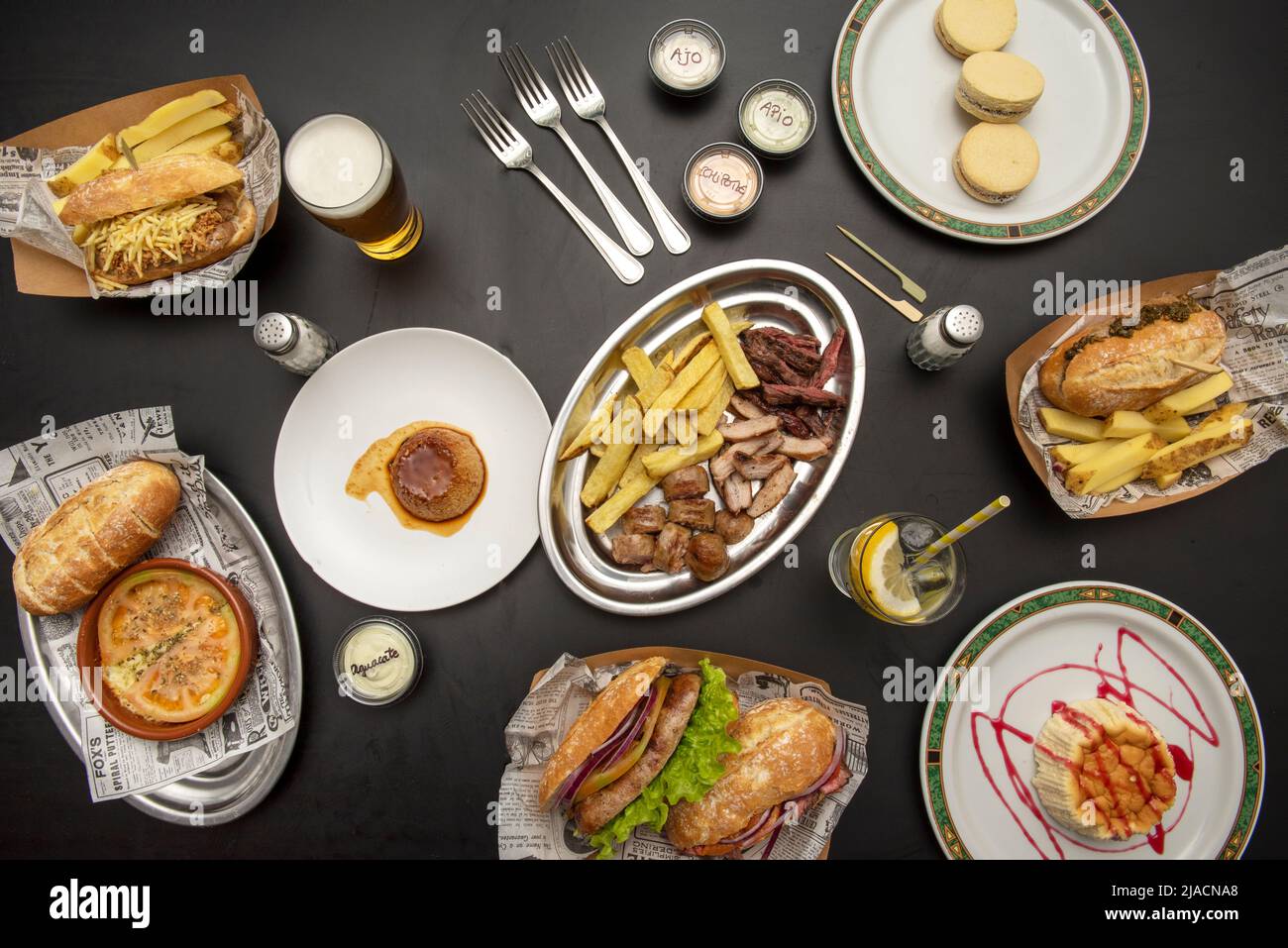 Auswahl an Tellern mit Sandwiches, pommes frites, Roastbeef in Scheiben, Panna Cotta, Eierpudding und Käsekuchen auf schwarzem Tisch Stockfoto