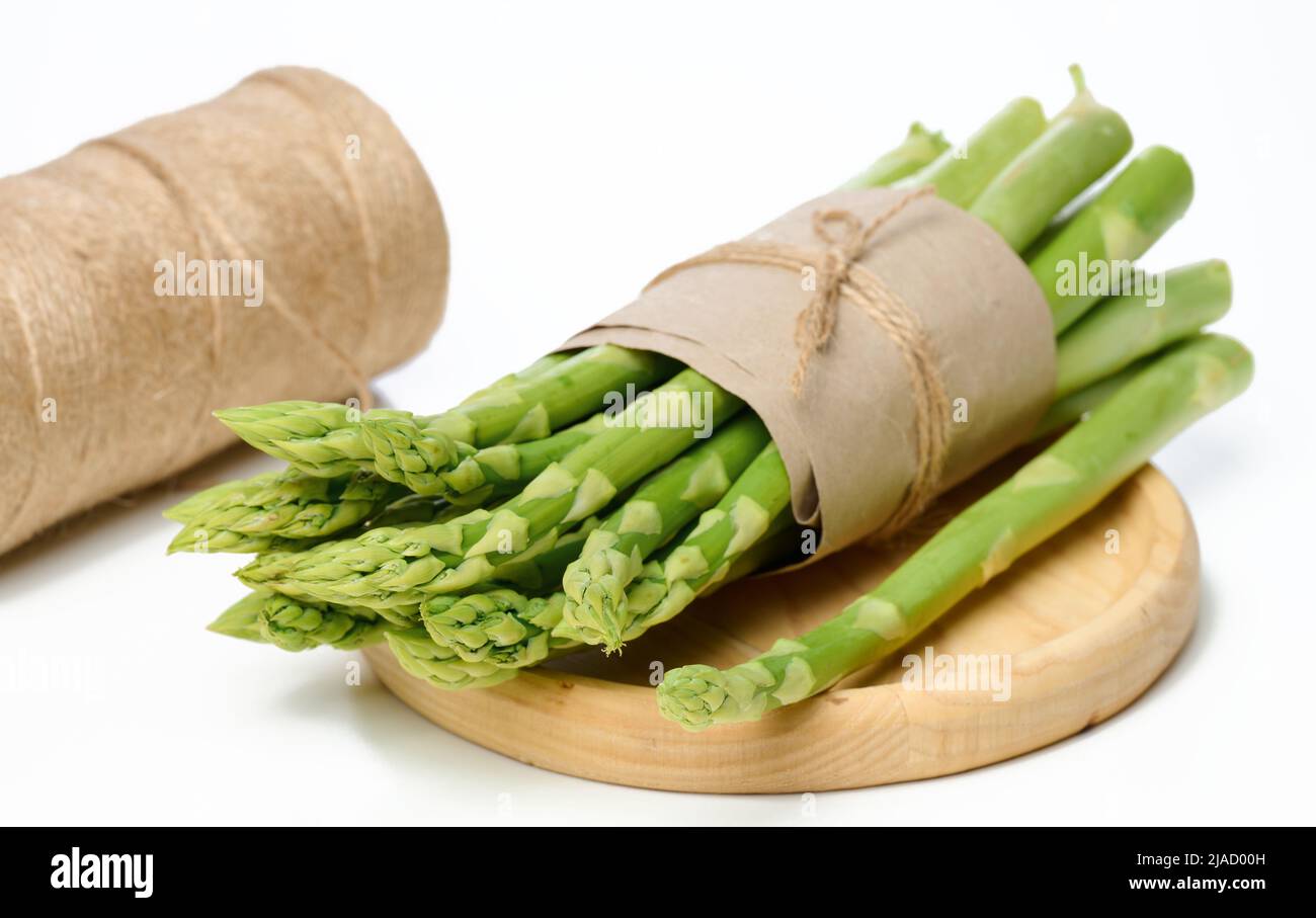 Auf einem Holzteller auf weißem Grund liegt ein paar frische Spargel in braunem Papier eingewickelt Stockfoto
