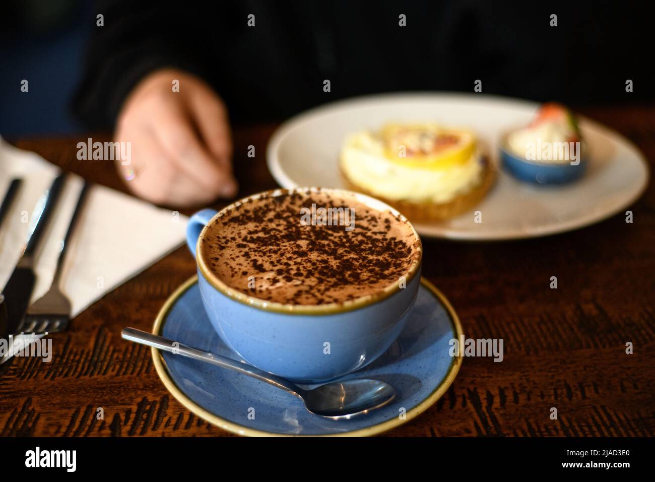Person, die an einem Tisch sitzt, bereit, eine Tasse heiße Schokolade mit Zitronencreme zu genießen Stockfoto